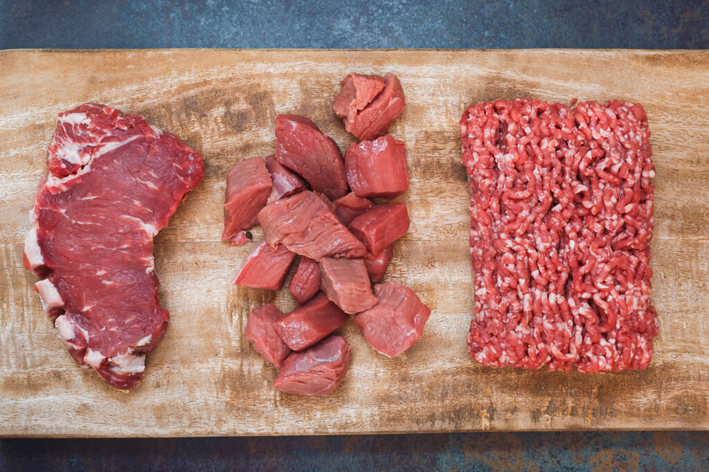 Different cuts of grass-fed beef meat: sirloin steak, ground and chopped meat on a wooden cutting board
